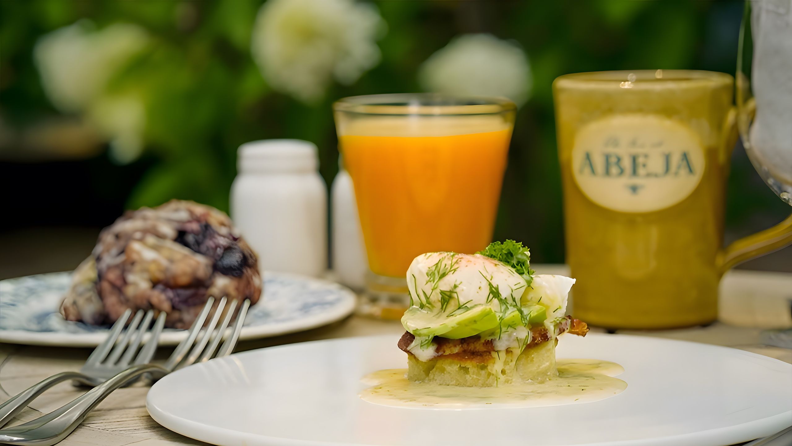 Breakfast spread of eggs Benedict, a cinnamon roll, and coffee in an Abeja-branded mug