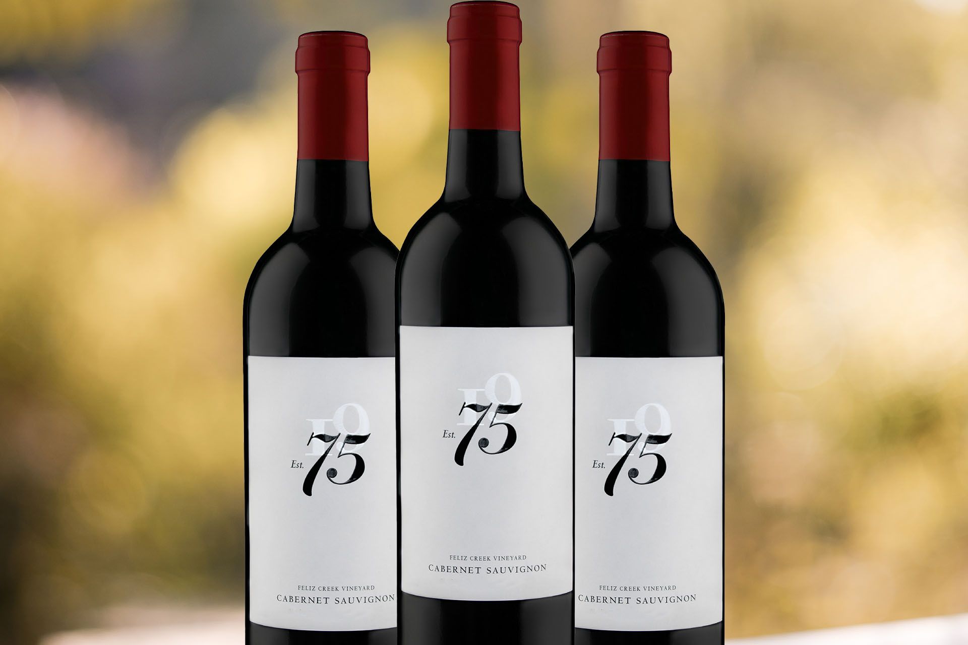 Three bottles of 75 Wine Co Feliz Creek Vineyard Cabernet Sauvignon with vineyard bokeh