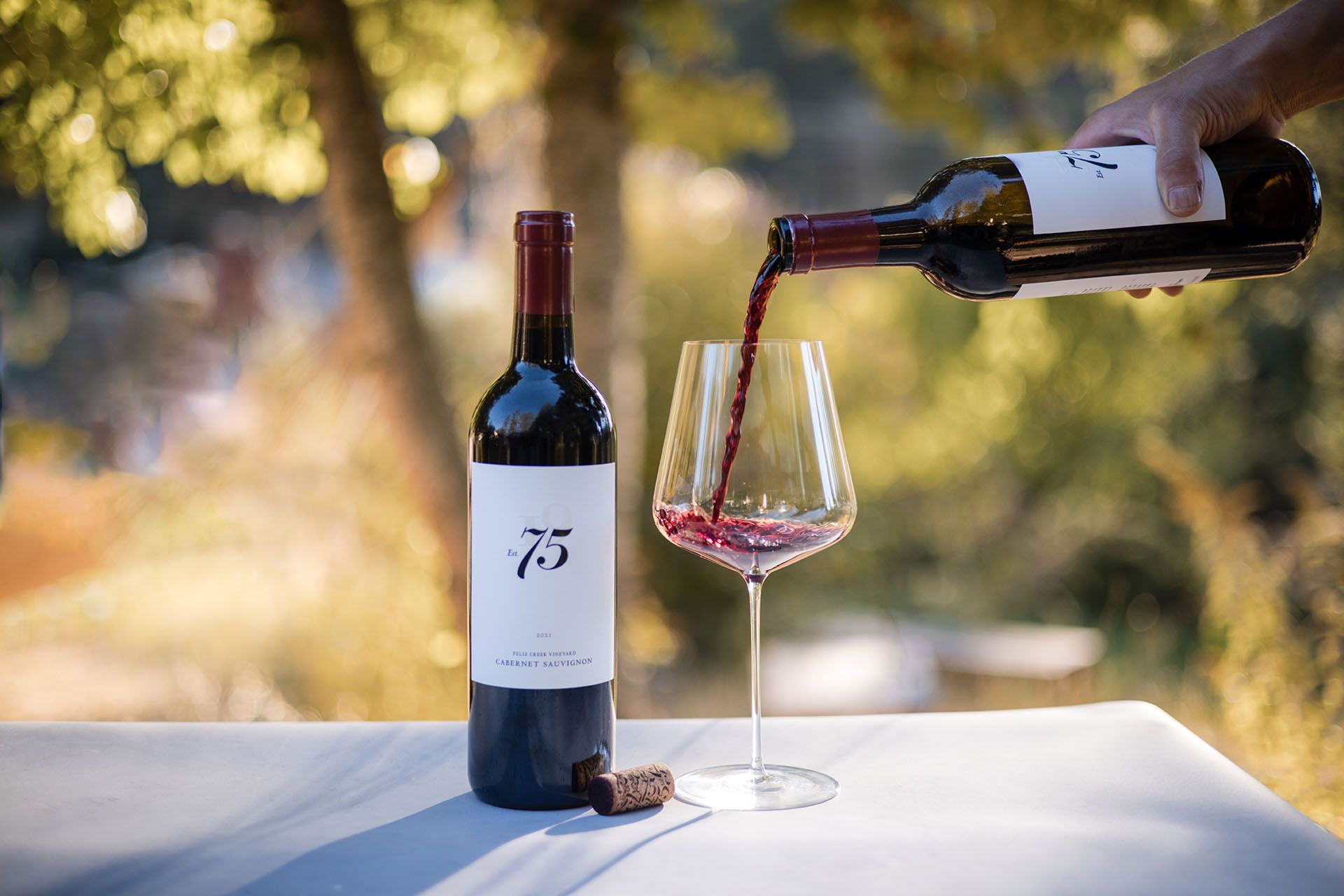 75 Wine Co Cabernet Sauvignon being poured into a glass in an outdoor vineyard setting