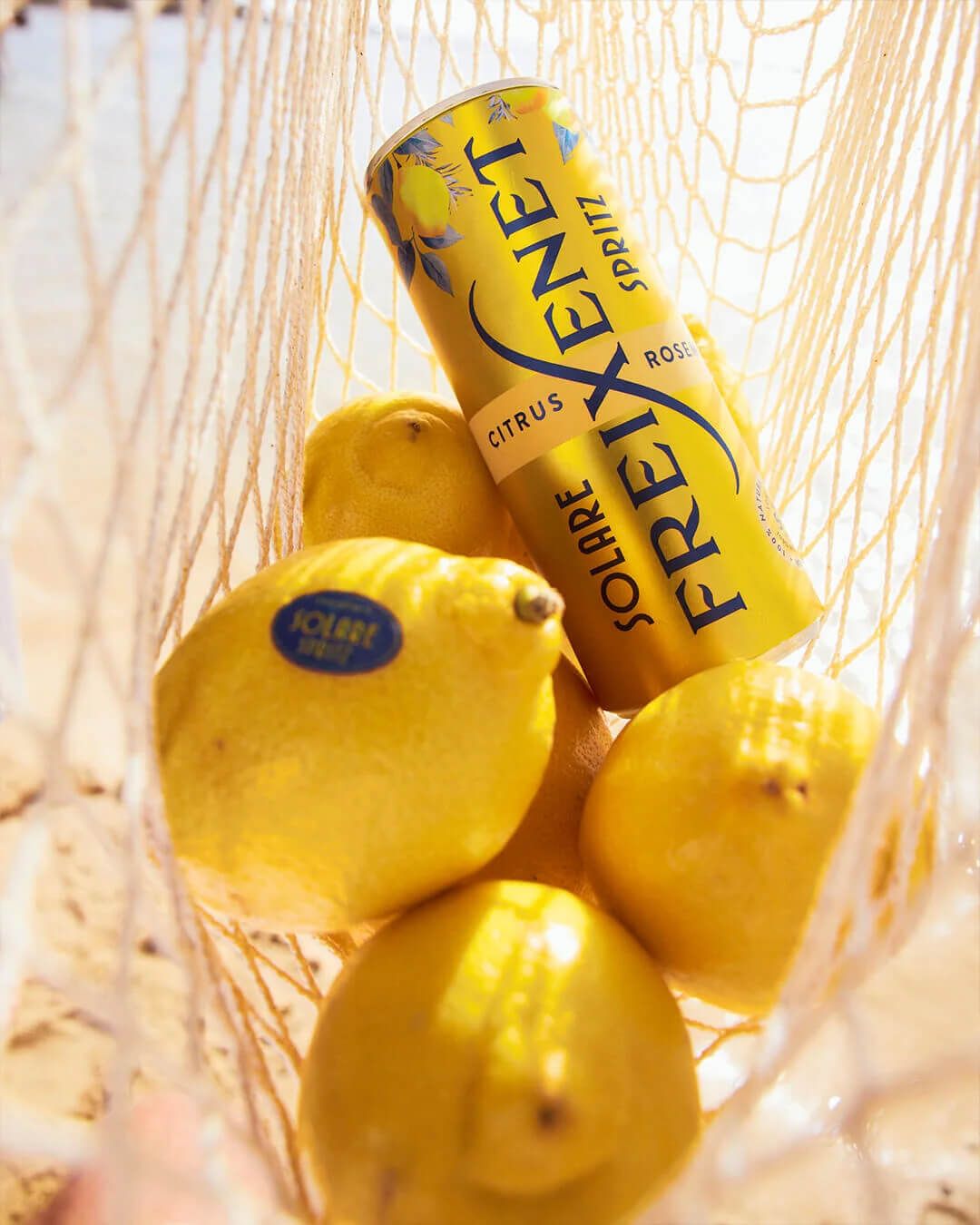 Freixenet Solare Spritz can tucked into a string bag of fresh lemons on a sunlit beach