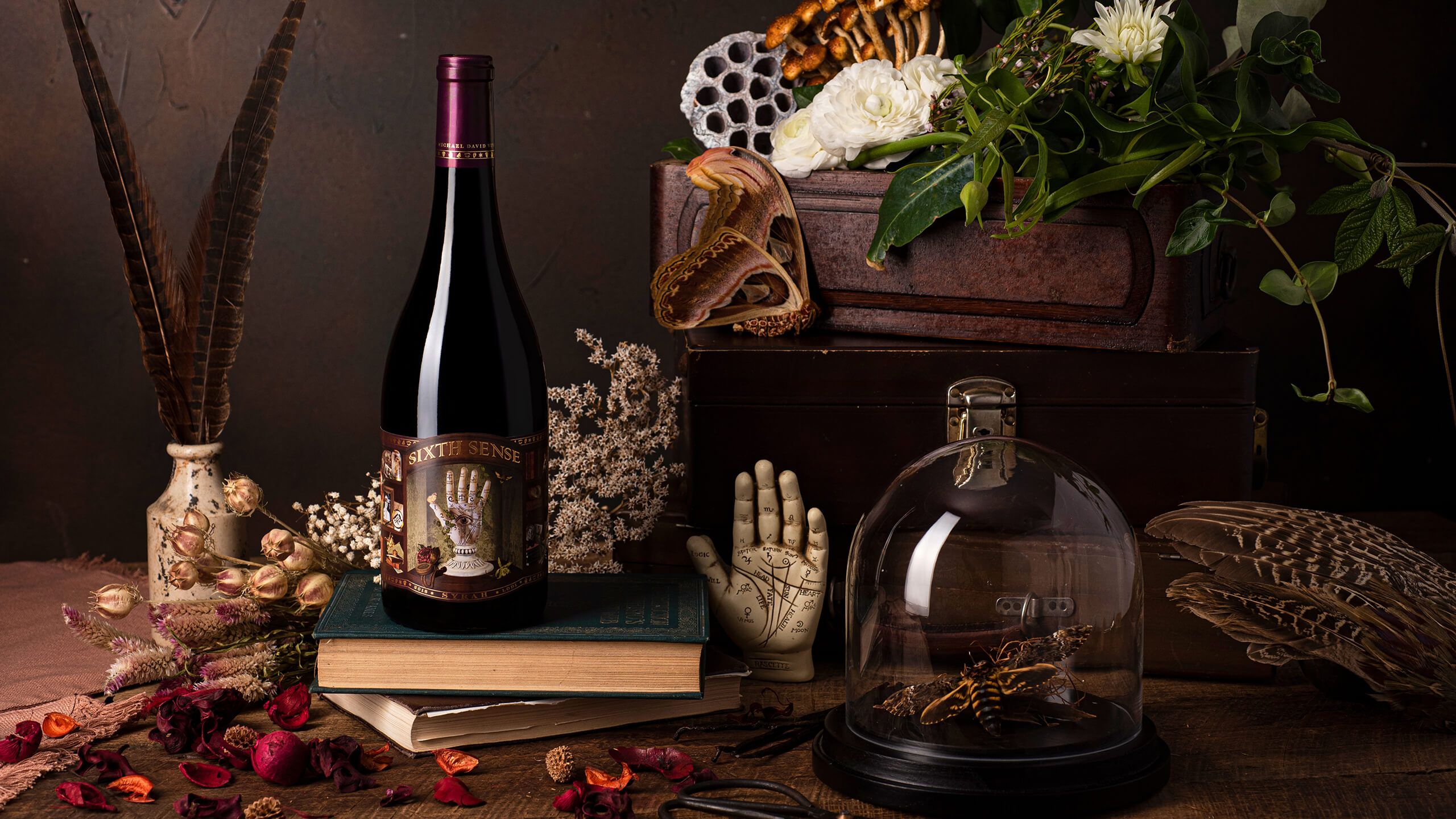 Current foiled 6th Sense Syrah bottle against a moody, dark cabinet-of-curiosities background